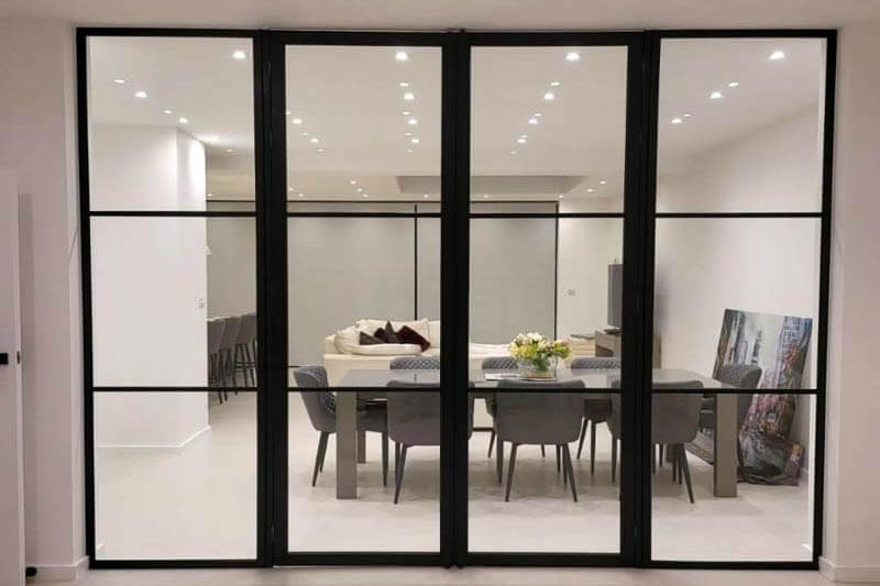 Black framed glazed screen and double doors between a hallway and a dining room