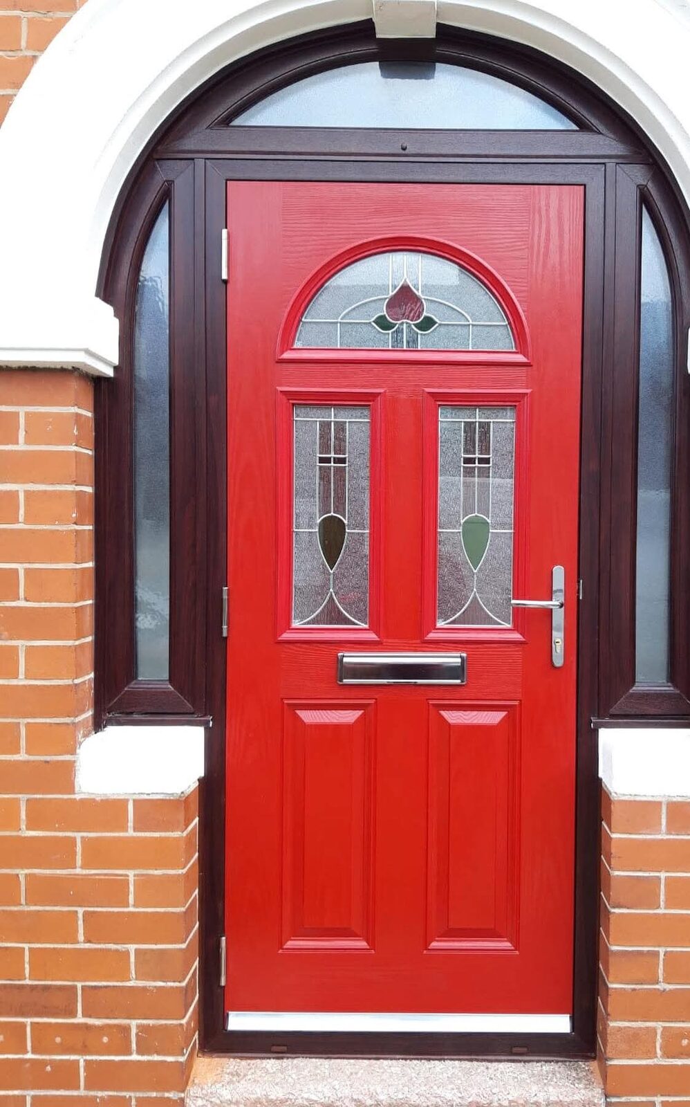 Red composite front door under a brick arch
